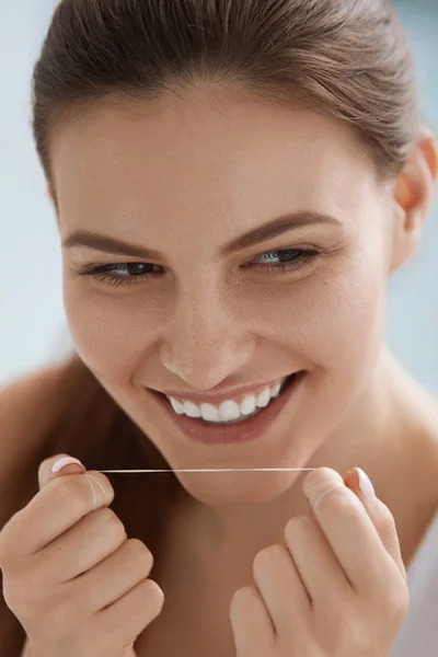 Hilo dental. Mujer sonriente limpiando dientes blancos con hilo dental — Foto de Stock