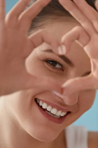 Eye health. Happy woman with smile and heart hands near eyes