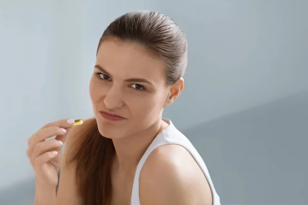 Medicine. Disgusted woman holding omega fish oil pill in hand