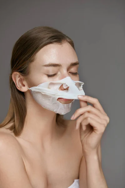 Gezichtsmasker. Vrouw het nemen van wit blad masker uit de huid van het gezicht — Stockfoto
