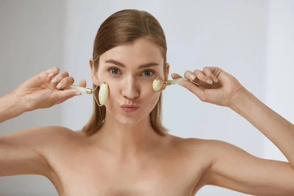 Cuidado de la cara belleza. Mujer haciendo masaje facial con rodillos de jade — Foto de Stock