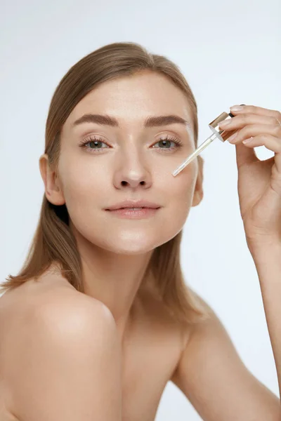 Skin care. Woman applying serum or facial oil on beauty face