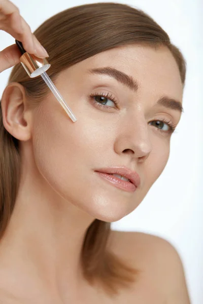 Cuidado de la piel. Mujer que aplica suero o aceite facial en la cara de belleza —  Fotos de Stock