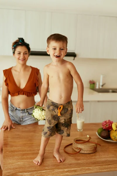 Mulher e criança se divertindo comendo vegetais na cozinha — Fotografia de Stock