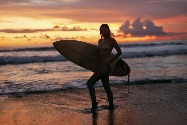 Surfermädchen mit Surfbrett am Strand bei Sonnenuntergang im Sommerurlaub — Stockfoto