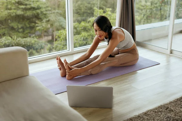 Yoga fitness. Chica estirando el cuerpo en casa usando la computadora — Foto de Stock