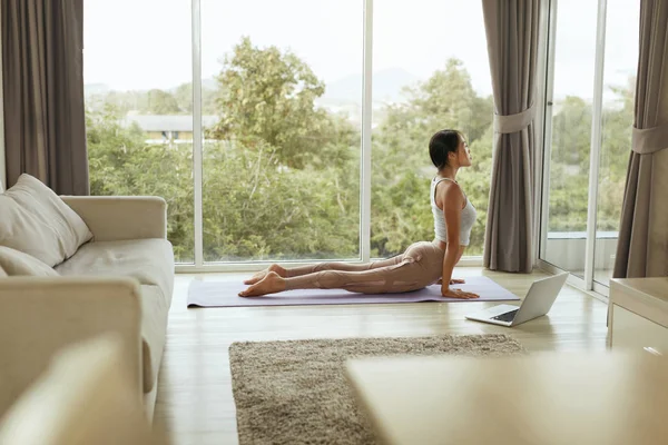 Chica haciendo entrenamiento de yoga, estirando el cuerpo en casa con el ordenador — Foto de Stock