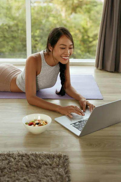 Smiling girl using computer sitting on floor at home in morning — Stock Photo, Image