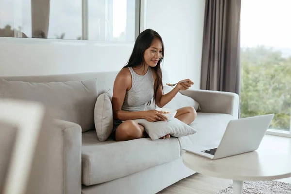 Kvinna som har frukost när du använder datorn hemma i morse — Stockfoto