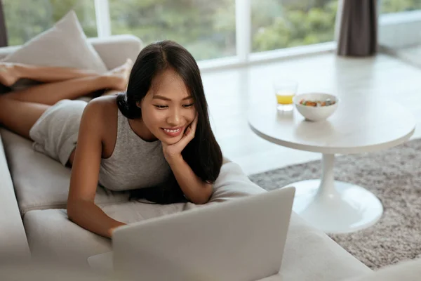 Mulher com computador portátil no sofá na sala de estar em casa — Fotografia de Stock