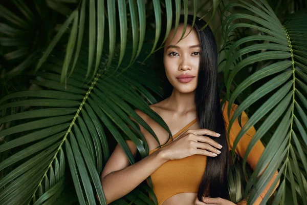 Haarschönheit. Frau Modell mit langen glatten Haaren in Palmblättern — Stockfoto