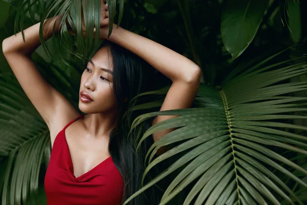 Fashion. Asian woman model in red dress with green palm leaves — Stock Photo, Image