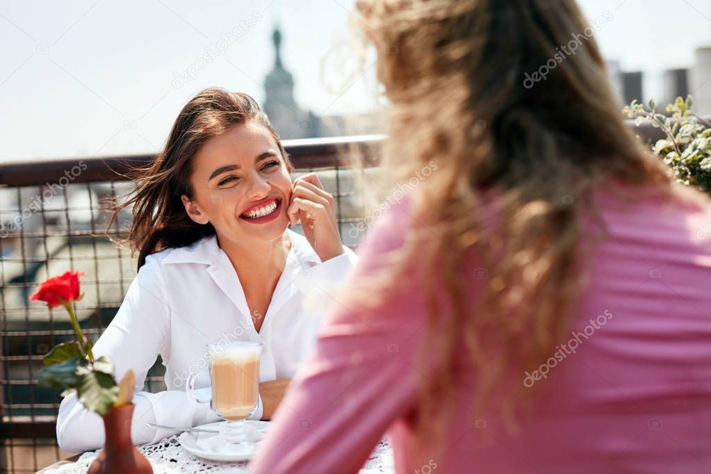 Woman Drinking Coffee In Cafe With Friend Outdoors