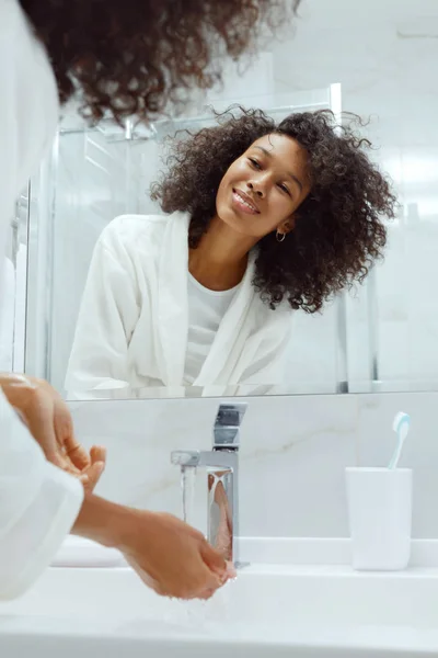 Szczęśliwa kobieta myje ręce w zlewie patrząc w lustro w łazience — Zdjęcie stockowe