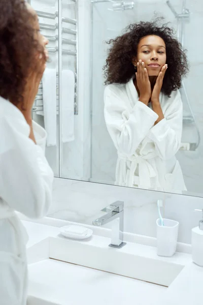 Cuidado de la piel. Mujer tocando la cara, mirando el espejo en el baño — Foto de Stock