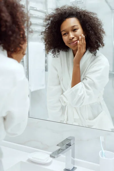 スキンケア。女性の顔に触れると、バスルームで鏡を見て — ストック写真