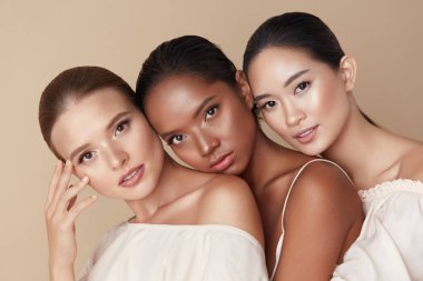Beauty. Group Of Diversity Models Portrait. Multi-Ethnic Women With Different Skin Types Posing On Beige Background. Tender Multicultural Girls Standing Together And Looking At Camera.   clipart