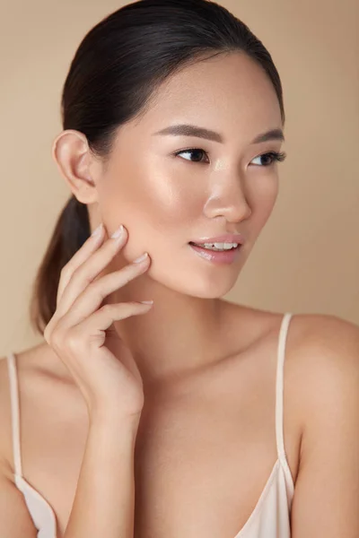 Woman. Skin Care For Perfect Look. Portrait Of Asian Model With Smooth Skin Touching Her Face And Looking Away. Female Enjoying Hydrated Skin After Daily Beauty Routine Or Cosmetology Treatment.