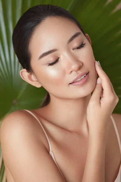 Beauty. Model Face On Palm Background. Asian Woman With Closed Eyes Enjoying Smooth, Hydrated And Glowing Skin. Organic Cosmetic And SPA Treatment For Perfect Body And Wellness.