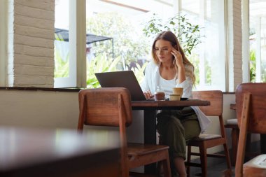 - Kadın. Cafe 'de online iş. Günlük kıyafetli güzel kız laptopta çalışıyor ve kafaya dokunuyor. Uzak İş veya Eğitim İçin Modern Dijital Teknolojiler.