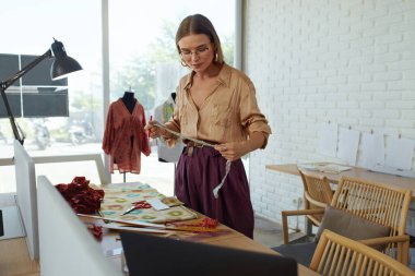 İş. Moda Tasarımcısı Atölyede. Yeni Elbise İçin Güzel Terzi Ölçümü Kumaşı. Atıcı 'da çalışan başarılı, şık giyimli, serbest çalışan kadın. Kendi Stüdyomuzda Profesyonel Terzi.