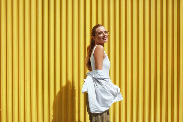 Женщина. Портрет сексуальной модели. Девушка из моды в повседневной одежде, стоящей против желтого металлического забора. Женщина в белой рубашке и топ-танке смотрит в камеру . — стоковое фото