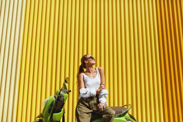 Urbano. Ragazza di moda sul ritratto di ciclomotore. Modello sexy in abiti casual e occhiali da sole contro recinzione in metallo giallo. Bella donna su Personal City Transport. — Foto Stock