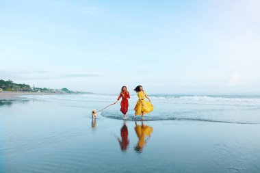 Kumsal. Kadınlar ve Köpek Çıplak Ayakla Okyanusta Yürüyor. Maksimum Giysili Moda Kızları Tropikal Deniz 'de Dinleniyor. Yaz Tatilinde Mükemmel Görünüm İçin Bohem Kıyafet Biçimi.