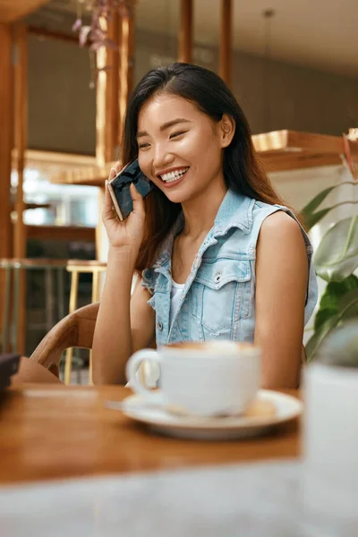 コーヒーショップで電話で話す女の子 カフェでスマホを持っている女性 通信のための夏休みに現代の技術を使用してカジュアル服で美しいアジアモデル — ストック写真