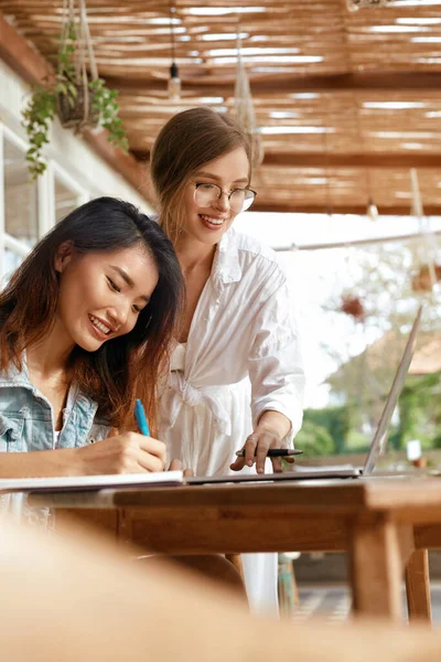 Girls At Coffee Shop. Women With Laptop Having Discussion About Business. Beautiful Colleagues In Casual Clothes Working Remotely At Cafe On Summer Vacation.