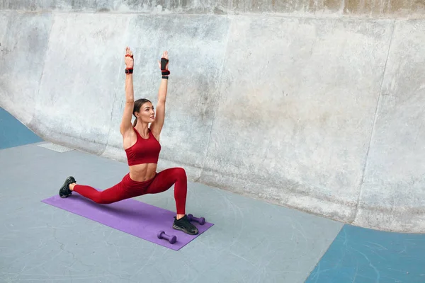 Vilken sport. Fitness Girl gör stretching träning på yogamatta. Mode Sportig kvinna med stark muskulös kroppsträning mot betong vägg bakgrund. Passar kvinnliga Stretching på Outdoor Stadium. — Stockfoto