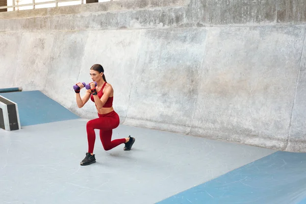 Desporto. Mulher se agacha contra a parede de concreto. Garota de fitness com corpo muscular forte na moda roupas esportivas trabalhando no estádio ao ar livre. Estilo de vida urbano e pessoas ativas . — Fotografia de Stock