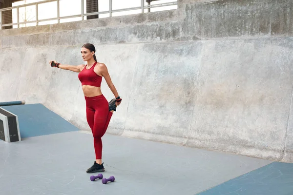 Entrenamiento. Chica de fitness estiramiento y preparándose para hacer ejercicio en el estadio al aire libre. Mujer sexy con fuerte cuerpo muscular en entrenamiento de ropa deportiva de moda contra la pared de hormigón . — Foto de Stock