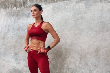 Fitness Kız Portresi. Moda sporu yapan kadın idmandan sonra taş duvara yaslanıyor. Güçlü kaslı vücudu olan, ellerini kalçasında tutan ve uzaklara bakan bir kadın..