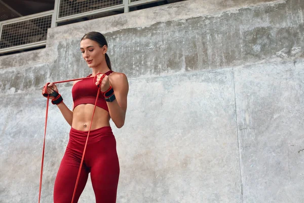 Una donna. Allenamento della banda di resistenza per un corpo muscolare forte. Fitness Girl In Fashion Sporty Outfit Fare esercizio contro il muro di pietra sullo stadio. Lo sport come stile di vita per le persone urbane. — Foto Stock