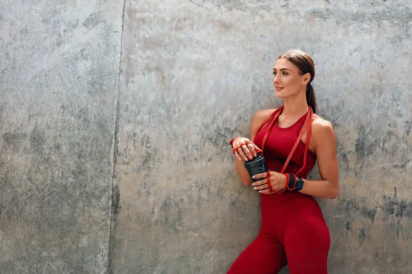 Chica Fitness Descansando. La mujer en forma en traje deportivo de moda con botella de cóctel de proteína tiene descanso después de un entrenamiento intenso. Ejercicio exterior urbano para un cuerpo muscular fuerte y un estilo de vida saludable . —  Fotos de Stock