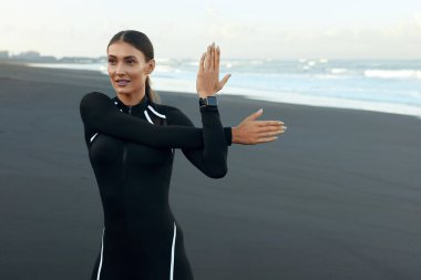 Plajdaki Fitness Kızı Portresi. Formda, spor kıyafetli, esneme egzersizi yapan ve başka tarafa bakan bir kadın. Tropikal Okyanusta Aktif İnsanlar İçin Yaşam Tarzı Olarak Sabah Çalışması.