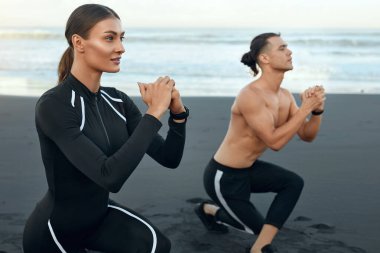 Sahilde çömelmiş spor çifti. Yakışıklı Adam ve Seksi Kadın Moda Sportif Kıyafet Eğitiminde. Gençler Sandy Coast 'ta antrenmandan önce ısınıyor. Yaşam Tarzı Olarak Aktif Tatil.