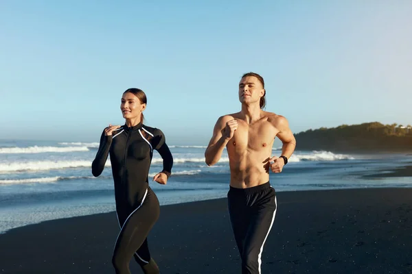 Playa. Hombre y mujer corriendo durante el entrenamiento al aire libre. Pareja Deportiva En Moda Ropa Deportiva Entrenamiento Por La Mañana. Ejercicio de jogging cerca del océano en vacaciones de verano como parte de un estilo de vida activo . — Foto de Stock