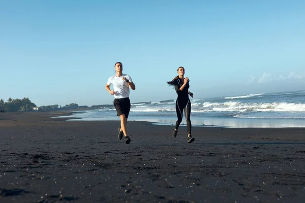 Playa. Pareja deportiva corriendo durante el entrenamiento matutino. Hombre guapo y mujer sexy en entrenamiento de ropa deportiva de moda en la costa. Vacaciones de verano activas en el océano tropical como estilo de vida . —  Fotos de Stock