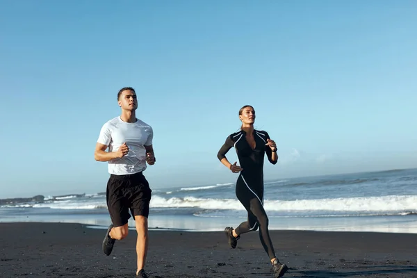 Plage. Femme et homme courent le long du littoral. Couple de sport dans la mode Sportswear sur l'entraînement en plein air le matin. Jogging Exercice près de l'océan en vacances d'été dans le cadre du mode de vie actif. — Photo