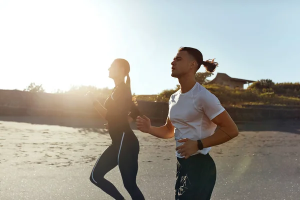 Sport On Beach. Running Couple In Fashion Sportswear On Morning Workout. Sexy Man And Beautiful Woman Jogging Along Ocean Coastline At Sunrise. Active Lifestyle On Summer Vacation At Tropical Resort.