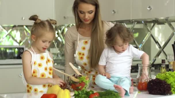 Frau mit Kindern kocht Gemüsesalat in der Küche — Stockvideo