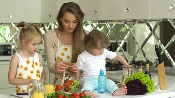 Frau mit Kindern kocht Gemüsesalat in der Küche — Stockvideo