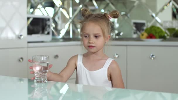 Trinken Sie Wasser. Kleines Mädchen trinkt Wasser aus Glas in der Küche — Stockvideo
