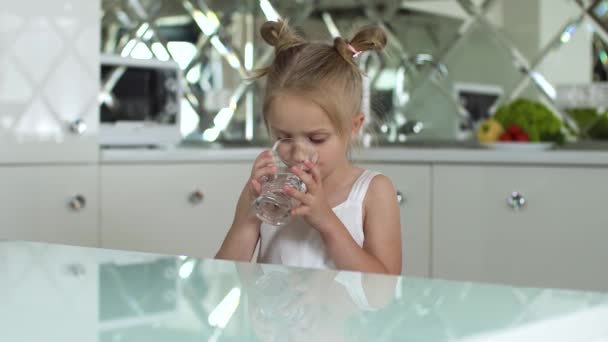 Beba água. Menina pequena água potável de vidro na cozinha — Vídeo de Stock