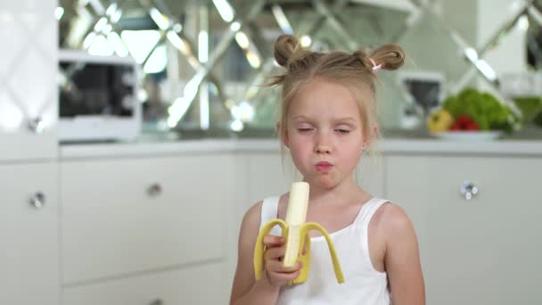 Дитина їсть їжу. Маленька дівчинка їсть банан на кухні — стокове відео