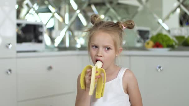 Kind isst Essen. Kleines Mädchen isst Banane in der Küche — Stockvideo