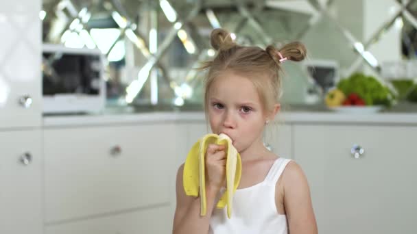 Jedzenie dzieci. Mała dziewczynka jedząca banana w kuchni — Wideo stockowe
