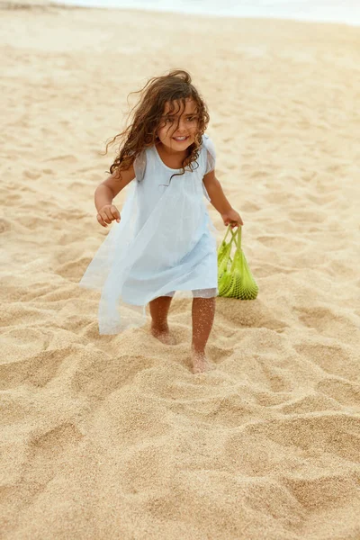 Summer. Kid On Beach Portrait. Cute Little Girl With Curly Hair Carrying Watermelon In Eco Bag. Natural Fruit And Organic Nutrients For Healthy Diet. Family Picnic On Sandy Coast.